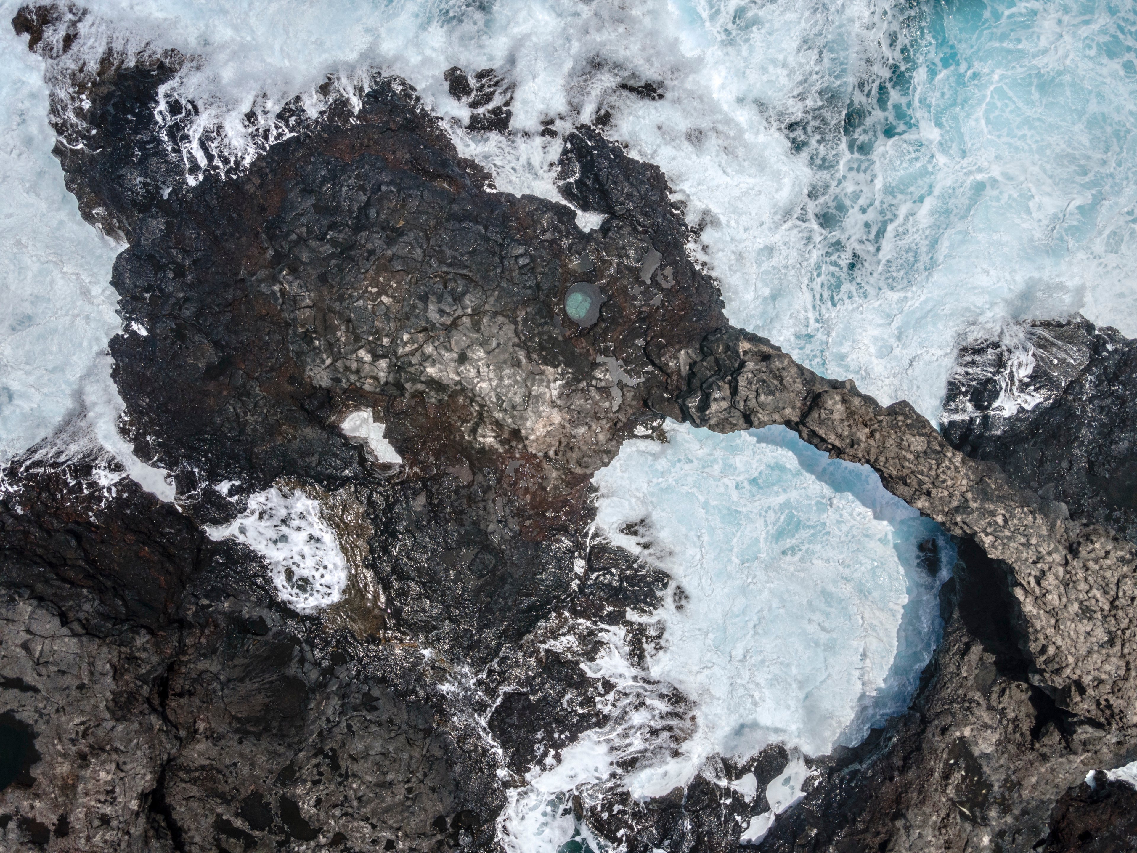 Dark rocky shore and white surf seen from above